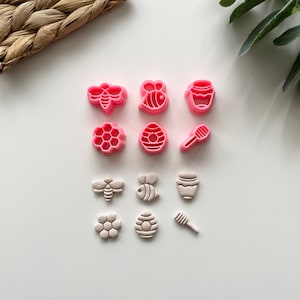 May include: A set of pink and white plastic cookie cutters shaped like bees, honeycombs, honey pots, and honey dippers.