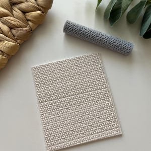 May include: A white silicone rolling pin with a geometric pattern. The rolling pin is on a white surface.