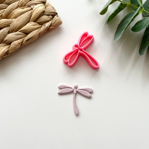 Può includere: Due tagliabiscotti a forma di libellula rosa. Uno è rosa scuro e l'altro è rosa chiaro.