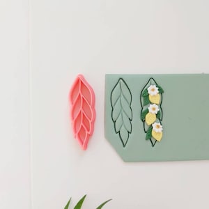 Könnte beinhalten: Ein rosa blattförmiger Ausstecher und eine grüne Silikonform mit einem Blatt- und Zitronenblütenmuster.