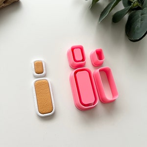 Op de afbeelding: Een set van vier roze plastic koekjesuitstekers in de vorm van rechthoeken. De uitstekers zijn in een rij gerangschikt, met de grootste uitsteker links en de kleinste uitsteker rechts. De uitstekers worden gebruikt om vormen te maken voor koekjes, fondant of andere eetbare ambachten.