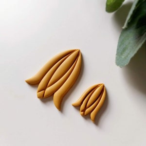 May include: Two yellow clay flower shapes, one larger than the other, on a white background.