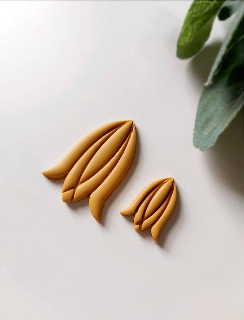 May include: Two yellow clay flower shapes, one larger than the other, on a white background.