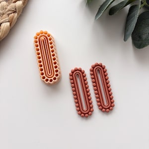 Può includere: Tre fustelle ovali in argilla polimerica nei toni del pesca e terracotta. Una è uno stampo, le altre due sono pezzi finiti. Le fustelle hanno un bordo perlato e un ritaglio ovale centrale, per progetti creativi.