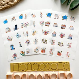 Può includere: Adesivi ad acquerello con illustrazioni floreali e a tema autunnale, insieme a un set di taglierini in argilla polimerica rosa chiaro di varie forme. È presente anche un taglierino rettangolare giallo.