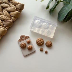 Peut inclure: Divers boutons bruns texturés de différentes tailles, ainsi qu'un moule en silicone transparent. Les boutons sont disposés sur une surface blanche avec une étiquette en bois. Les boutons ont un motif quadrillé.