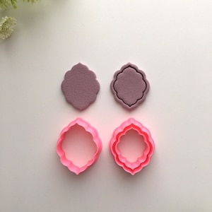 May include: Two sets of pink plastic cookie cutters in the shape of a decorative frame. The cutters are layered, with a smaller frame inside a larger frame.