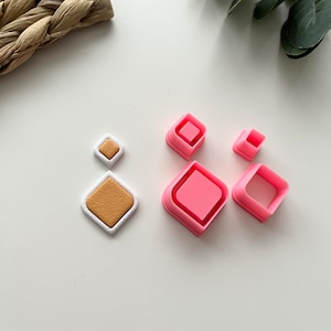 May include: Set of five pink plastic diamond-shaped cookie cutters. The cutters are of varying sizes.