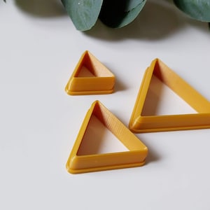 Puede incluir: Tres cortadores de galletas en forma de triángulo de diferentes tamaños, de color dorado.