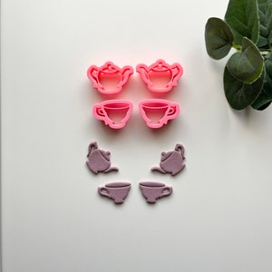 May include: A set of six pink and purple plastic cookie cutters shaped like teapots and teacups.