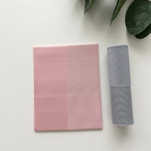 Op de afbeelding: Een roze en grijs gestreept, getextureerd papier met een verticale lijn die de twee kleuren scheidt. Het papier ligt op een wit oppervlak.