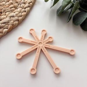 May include: A set of light peach-colored, 3D-printed measuring tools, each with a circular end and a labeled arm. Measurements range from 20mm to 55mm. The tools are arranged in a starburst pattern on a white surface.