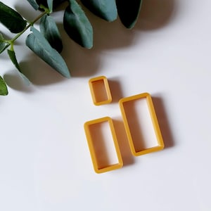 Puede incluir: Tres cortadores de galletas de plástico amarillo en forma de rectángulos, dispuestos en orden decreciente de tamaño.