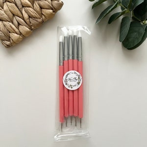 Puede incluir: Un conjunto de seis herramientas de escultura de color rosa y plateado con puntas de silicona blanca, empaquetadas en una bolsa de plástico transparente. Las herramientas están etiquetadas con el texto "Vee Clay Designs".