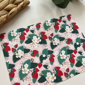 May include: Pink fabric with a repeating pattern of red strawberries, green leaves, and white flowers.