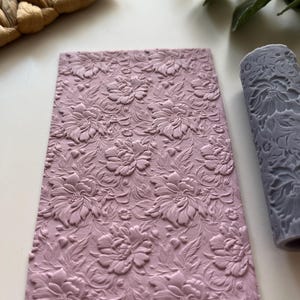 May include: A pink silicone rolling pin with a floral pattern. The rolling pin is used for decorating cakes and pastries.