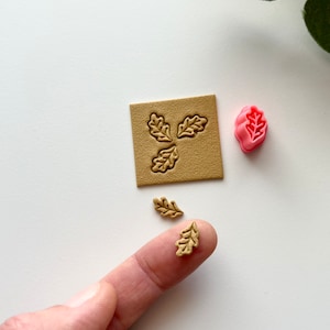 May include: A set of three leaf-shaped stamps, two are gold and one is pink. The stamps are on a white surface.