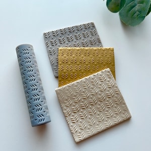 May include: A set of three textured rolling pins with a leaf pattern. The rolling pins are gray, gold, and beige.