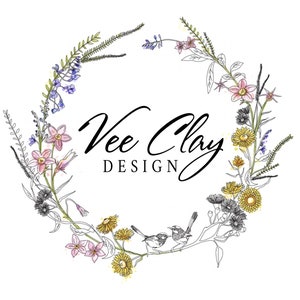 May include: A wreath of wildflowers and greenery with two small birds perched on a branch. The wreath is in shades of pink, yellow, blue, and green. The text "Vee Clay DESIGN" is in the center of the wreath.