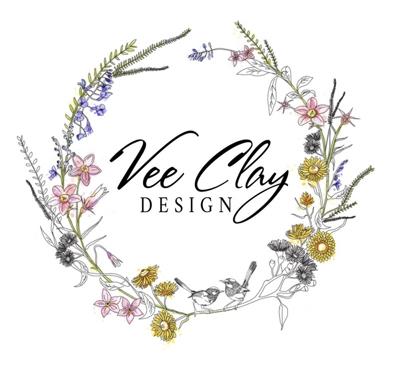 May include: A wreath of wildflowers and greenery with two small birds perched on a branch. The wreath is in shades of pink, yellow, blue, and green. The text "Vee Clay DESIGN" is in the center of the wreath.