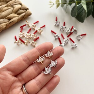 Può includere: Due paia di ciondoli per orecchini a forma di foglia di cristallo con montature dorate e argentate. I ciondoli sono mostrati su una mano con un anello.