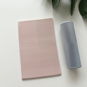 May include: A light pink rectangular tray with a herringbone pattern and a light grey cylindrical container with a similar pattern.