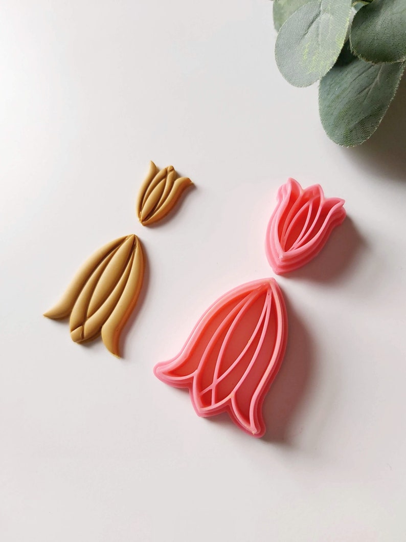 May include: Two sets of flower-shaped cookie cutters. One set is pink and the other is gold.