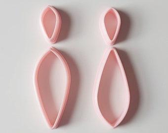 Può includere: Un paio di orecchini pendenti rosa a forma di lacrima. Gli orecchini sono composti da due pezzi di plastica, uno dentro l'altro.