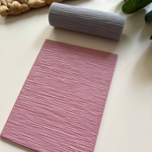 Puede incluir: Un sello de goma texturizado rosa con un patrón de veta de madera. El sello es rectangular y tiene una superficie lisa.