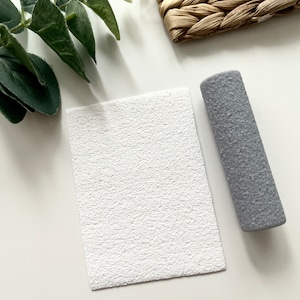 Puede incluir: Una hoja de cartulina blanca texturizada con un rodillo gris texturizado a su lado.