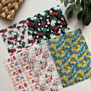 May include: Five different patterned fabric sheets with various designs, including strawberries, lemons, seashells, and flowers. The sheets are arranged in a stack on a white surface.