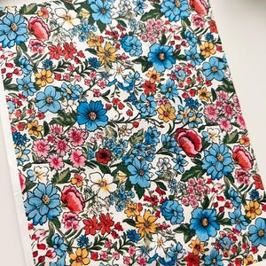 Puede incluir: Un estampado floral con una densa disposición de flores coloridas. El diseño incluye flores azules, rojas, amarillas y rosas sobre un fondo blanco. Las flores están detalladas con hojas y tallos verdes.