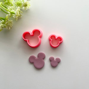 Peut inclure: Deux emporte-pièces en plastique rose en forme de tête de Mickey Mouse et deux têtes de Mickey Mouse en fondant violet.