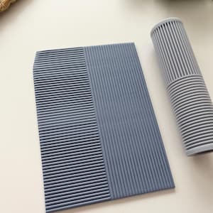 May include: A set of two gray textured items. One is a rectangular pad with vertical and horizontal ribbed detailing. The other is a cylindrical roller with ribbed detailing. Both items are on a white surface.