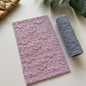 May include: A set of two pink silicone rolling pins with a floral pattern. The rolling pins are used for decorating fondant, clay, or other crafts.