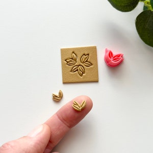 Puede incluir: Un conjunto de tres sellos de arcilla polimérica en forma de hoja. Los sellos son en tonos marrones y rosados. Los sellos se utilizan para crear impresiones en arcilla o fondant.