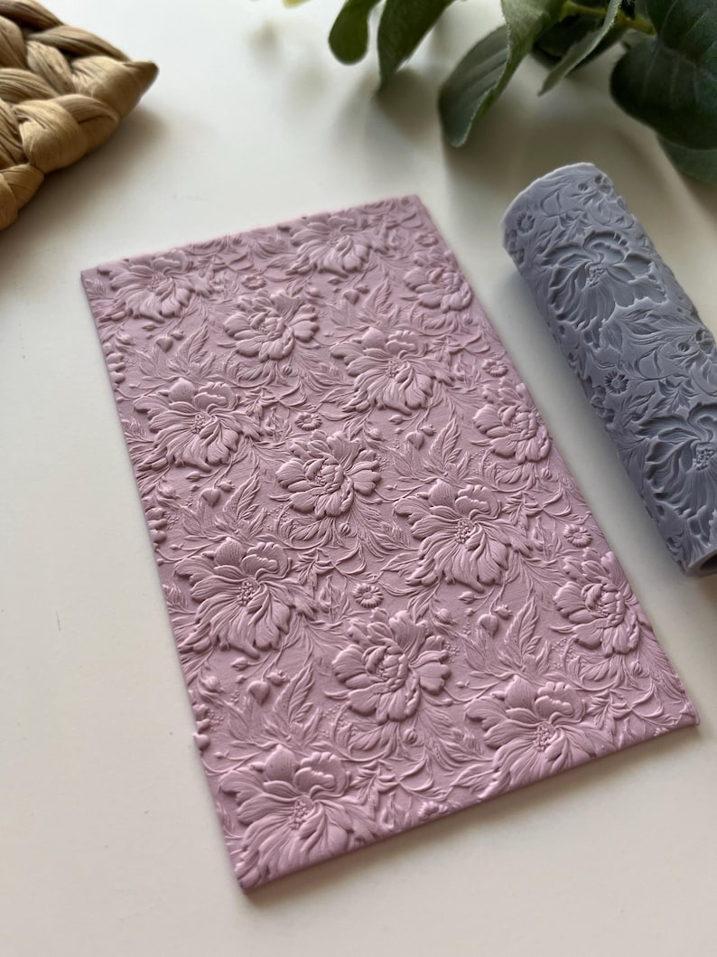 May include: A light purple silicone rolling pin with a floral design. The rolling pin is used for creating embossed patterns on fondant or clay.