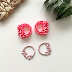 May include: A set of four pink resin earrings featuring a wreath design with leaves. The earrings are in two different sizes.