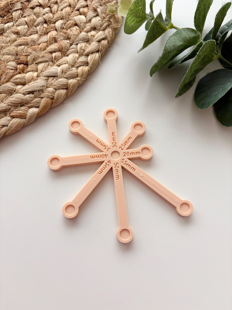 May include: A light peach-colored tool with multiple arms, each labeled with a measurement in millimeters. The tool is designed for measuring, with measurements ranging from 20mm to 55mm. The tool is on a white surface.