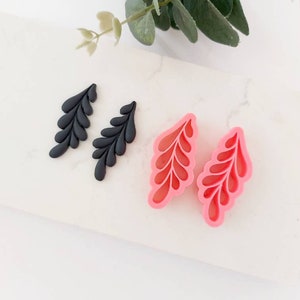 Könnte beinhalten: Zwei Paare von blattförmigen Silikonformen. Ein Paar ist schwarz und das andere Paar ist rosa.