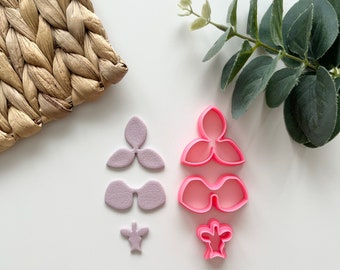 Può includere: Un set di tagliapasta in plastica rosa e viola a forma di fiore. I tagliapasta sono disposti in una pila verticale su una superficie bianca.