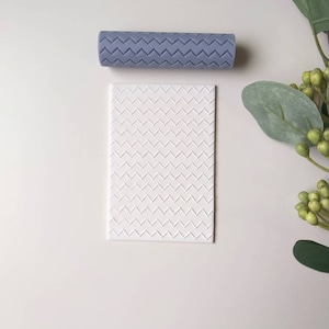 May include: A white silicone rolling pin with a chevron pattern and a matching silicone sheet with the same pattern.