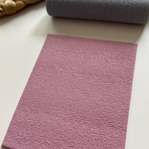 Puede incluir: Primer plano de una hoja de tela texturizada rosa. La tela tiene un sutil patrón tejido y una superficie suave y lisa.