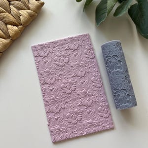 May include: A set of two pink and gray silicone rolling pins with a floral pattern. The rolling pins are used for creating embossed designs on fondant, clay, or dough.