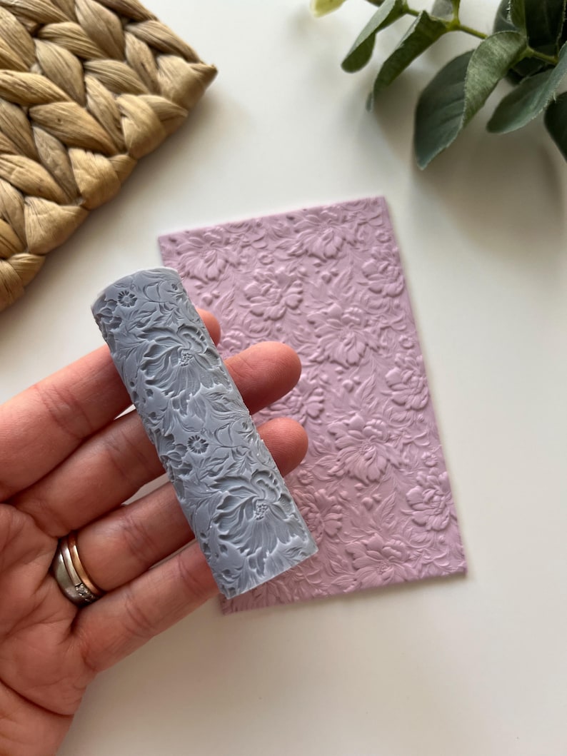 May include: A gray rolling pin with a floral design, next to a pink sheet of fondant with the same floral design embossed on it.