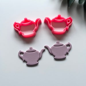 Puede incluir: Dos cortadores de galletas de tetera de plástico rosa y dos teteras de fondant morado.