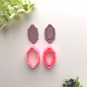 Può includere: Due set di stampini per biscotti, uno rosa e l'altro viola. Gli stampini hanno la forma di cornici ovali con bordi decorativi.