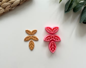 Può includere: Un set di due tagliabiscotti a forma di foglia. Un tagliabiscotti è rosa e l'altro è dorato.