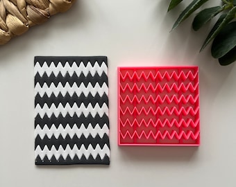 Puede incluir: Un molde de fondant con estampado de chevron blanco y negro y un molde de fondant de plástico rosa con chevron.
