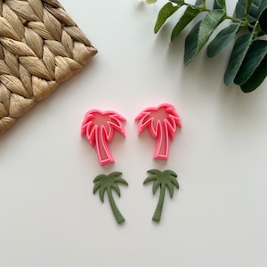 Puede incluir: Dos cortadores de galletas de palmera rosa y dos cortadores de galletas de palmera verde sobre una superficie blanca.